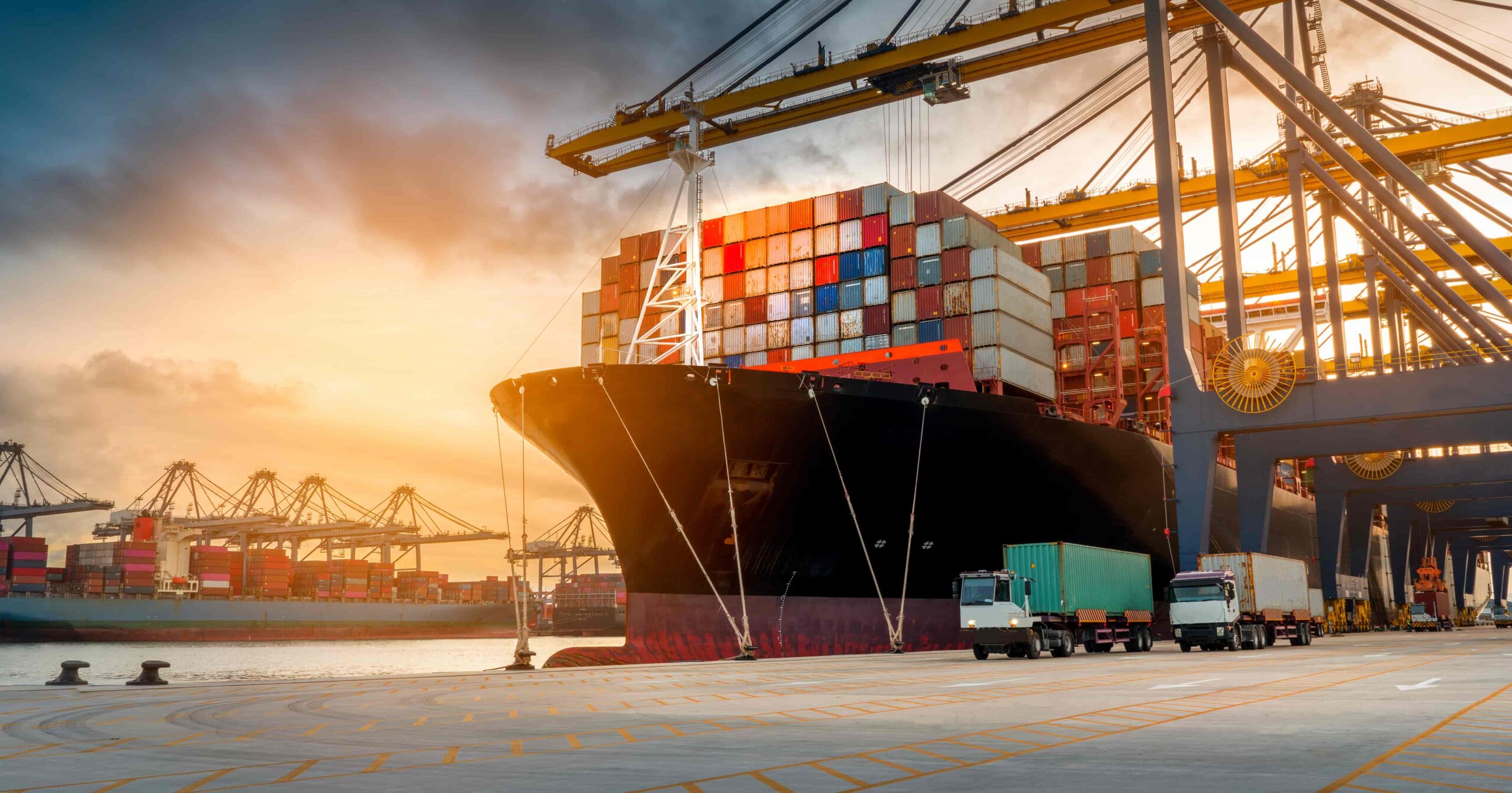 A large ship loaded with a large number of shipping containers docked in a harbor in the evening.