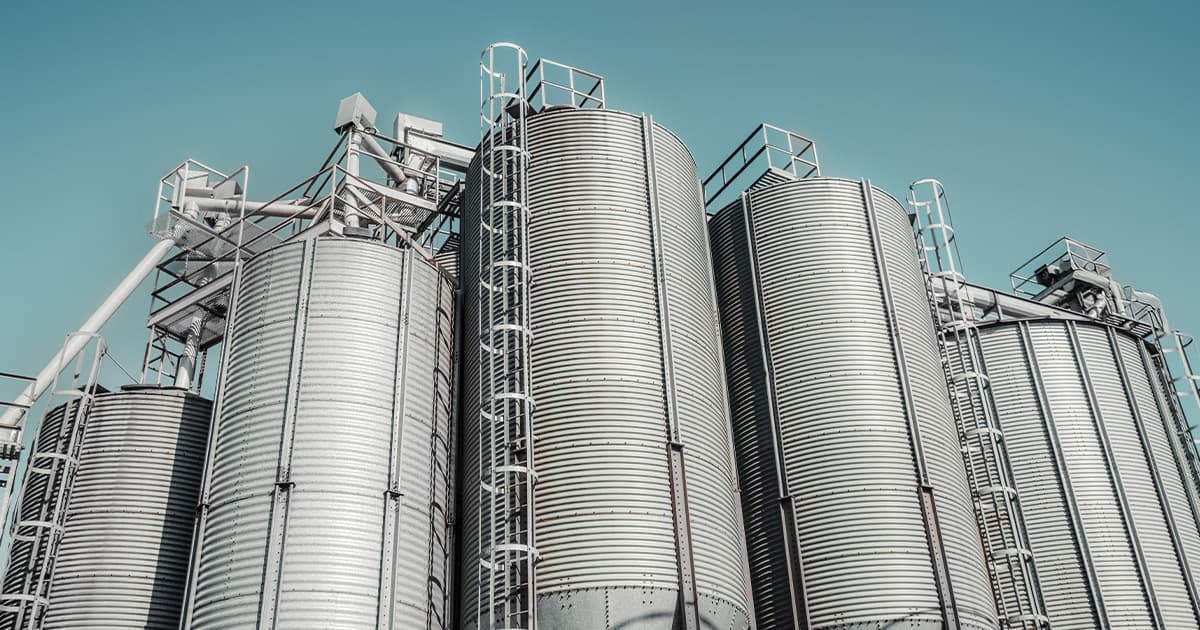 A low-angle view of large metal grain silos against a clear blue sky.
